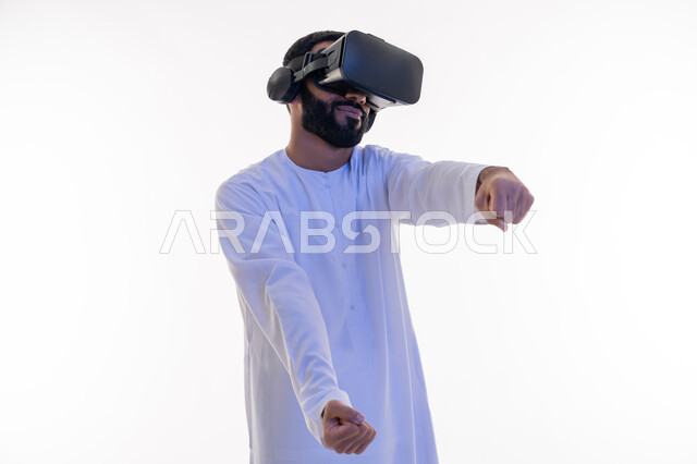 تقنيات وأجهزة تكنولوجية، إيماءات يدين تدل على السعادة بألعاب قيادة السيارات، محاكاة ركوب سيارة ثري دي في العالم الخيالي، بورتريه مقرب لرجل عربي خليجي اماراتي يرتدي الكندورة ونظارة الواقع الإفتراضي ثلاثية الأبعاد يقوم باللعب في ألعاب الفيديو، خلفية بيضاء