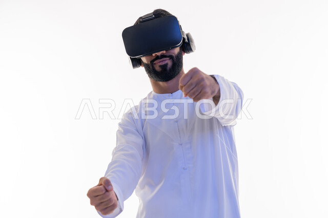 تقنيات وأجهزة تكنولوجية، إيماءات يدين تدل على السعادة بألعاب قيادة السيارات، محاكاة ركوب سيارة ثري دي في العالم الخيالي، بورتريه مقرب لرجل عربي خليجي اماراتي يرتدي الكندورة ونظارة الواقع الإفتراضي ثلاثية الأبعاد يقوم باللعب في ألعاب الفيديو، خلفية بيضاء