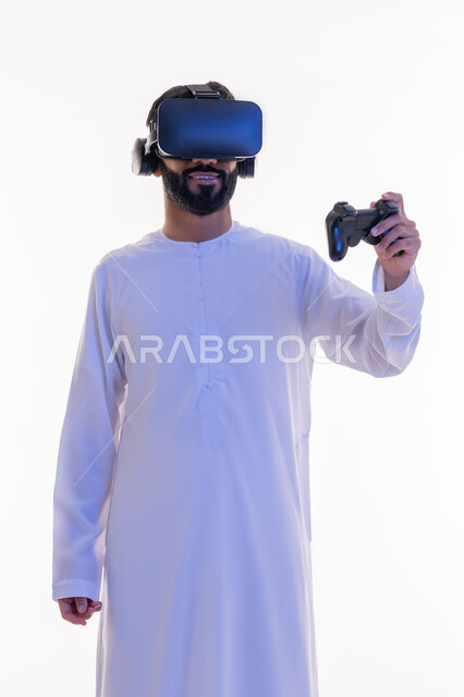 دمج العالم الخيالي مع المتعة والتسلية، أجهزة تكنولوجية وتقنيات حديثة، بورتريه لرجل عربي خليجي اماراتي مبتسم يرتدي الكندورة التقليدية ونظارة الواقع الإفتراضي يمسك بيده عصا التحكم يقوم باللعب في ألعاب الفيديو الترفيهية،  خلفية بيضاء