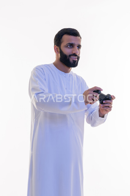 إيماءات الاندماج والتفاعل, مفهوم المتعة والتسلية، قضاء وقت ممتع في اللعب بألعاب الفيديو، الاستمتاع بالتقنيات والتكنولوجيا الحديثة، بورتريه لرجل عربي خليجي اماراتي يرتدي الكندورة يمسك بيده عصا التحكم، خلفية بيضاء