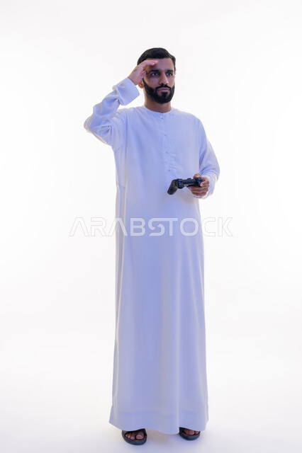 Expressions of sadness and loss, use of technological devices and modern techniques, portrait of an Arab Gulf Emirati man wearing a kandura and ghutra holding a joystick in his hand, playing recreational video games, full body, white background