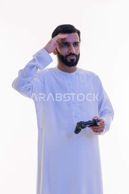 Expressions of sadness and loss, use of technological devices and modern techniques, portrait of an Arab Gulf Emirati man wearing a kandura and a ghutra holding a joystick in his hand, playing recreational video games, white background