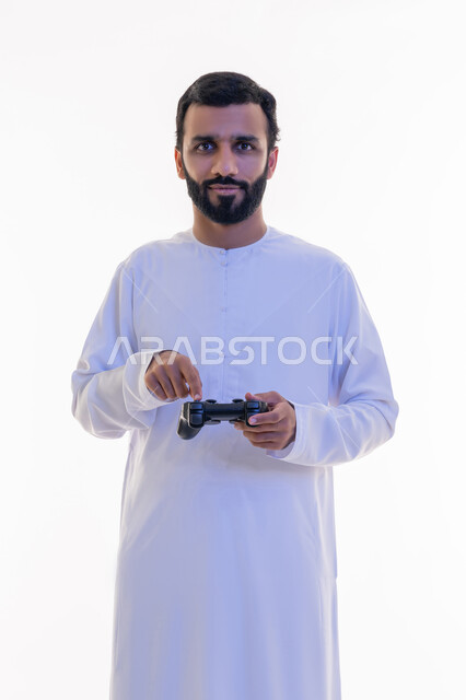 Playing entertaining video games, looking at the camera with confident expressions, gestures of enjoyment, integration and interaction, using technological devices and modern techniques, portrait of an Arab Gulf Emirati man wearing a kandura and ghutra clicking on a joystick, white background
