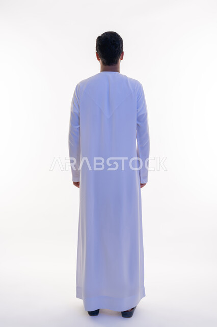 مفهوم الرجولة والقوة، الأناقة والاهتمام بالمظهر الخارجي، بورتريه من الخلف لرجل عربي خليجي إماراتي يرتدي الكندورة الاماراتية ينظر إلى شي ما، الوقوف باستقامة وثبات، الاعتراض عن موضوع محدد، الطول الكامل للجسم، خلفية بيضاء
