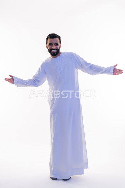 النظر إلى الكاميرا بإيماءات الثقة بالنفس، الاهتمام بالمظهر الخارجي, مفهوم الأناقة والرجولة, بورتريه لرجل عربي خليجي إماراتي مبتسم يرتدي الكندورة يرفع يديه إلى جانبيه بتعابير السرور والسعادة، الجسم بالطول الكامل، خلفية بيضاء
