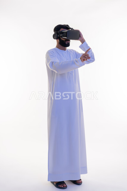 إيماءات الاندماج والاستمتاع، رفع إصبع السبابة للمس عناصر هولوجرلمية، مشاهدة الأفلام باستخدام تقنيات الواقع الافتراضي, محاكاة العالم الخيالي, بورتريه لرجل عربي خليجي إماراتي يرتدي الكندورة يضع نظارة ثلاثية الأبعاد، الجسم بالطول الكامل، خلفية بيضاء