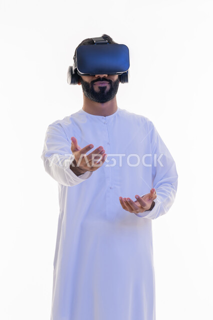 مشاهدة الأفلام باستخدام تقنيات الواقع الافتراضي, محاكاة العالم الخيالي, بورتريه لرجل عربي خليجي إماراتي يرتدي الكندورة يضع نظارة ثلاثية الأبعاد يقوم بالتحرك والتفاعل معها، رفع اليدين بإيماءات الاندماج والاستمتاع، خلفية بيضاء