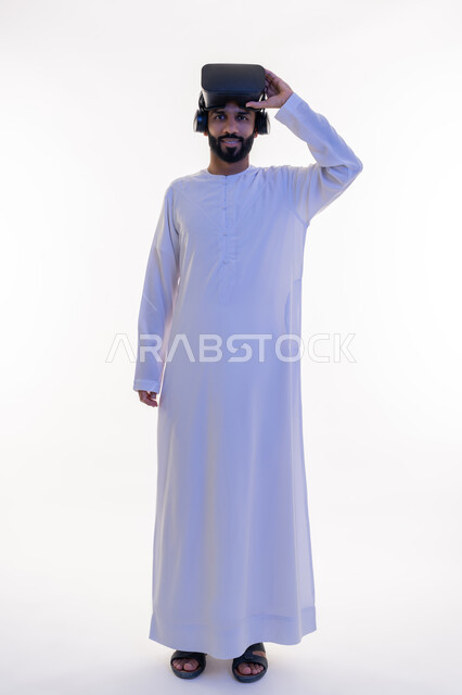 مشاهدة الأفلام باستخدام تقنيات الواقع الافتراضي, محاكاة العالم الخيالي, بورتريه لرجل عربي خليجي إماراتي يرتدي الكندورة يضع نظارة ثلاثية الأبعاد على رأسه ينظر إلى الكاميرا بإيماءات السرور، الجسم بالطول الكامل، خلفية بيضاء