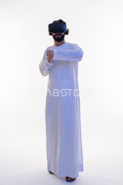 Practicing self-defense with technological techniques, portrait of an Arab Gulf Emirati man wearing a kandura and virtual reality glasses raising his hands with boxing and wrestling gestures, training in combat moves through video games, full body length, white background