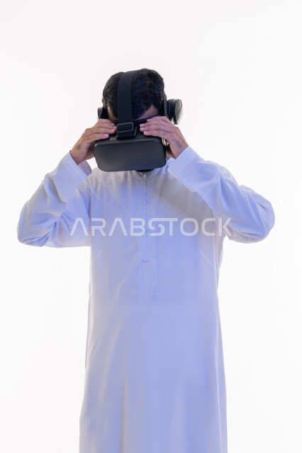 Fun and entertainment watching through virtual reality glasses, portrait of an Arab Gulf Emirati man wearing a kandura looking through 3D glasses with his hands on them, integration and simulation of the imaginary world, use of modern technical devices, technical and technological development, white background