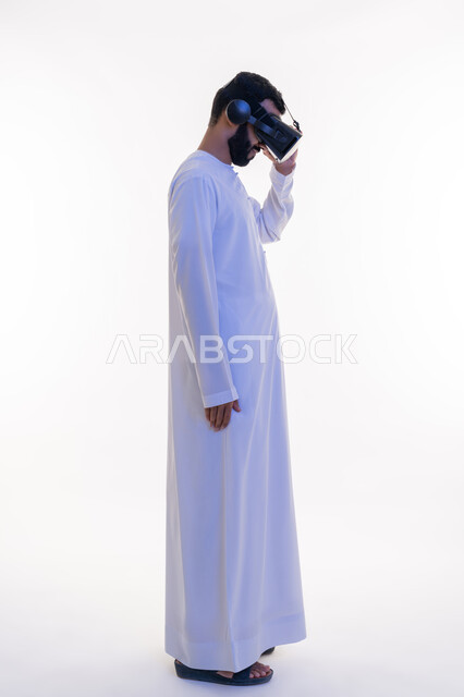 Fantasy world simulation, enjoying viewing through virtual reality glasses, side portrait of an Arab Gulf Emirati man wearing a kandura and 3D glasses with his hand on them, gestures of integration and concentration, use of modern technical devices, full-length body, white background