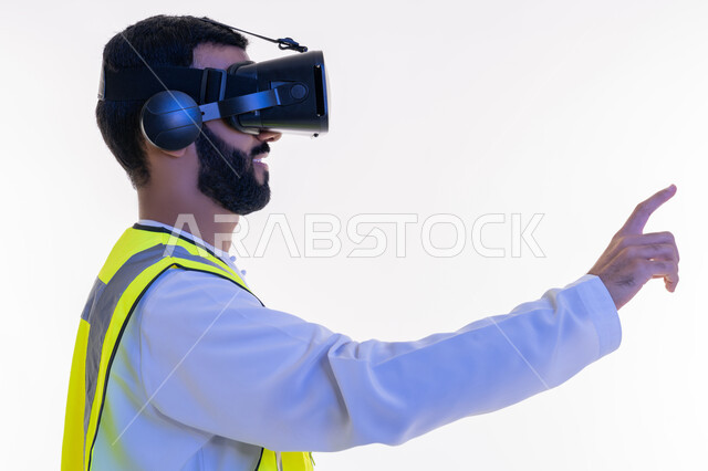 التفاعل مع الهندسة الافتراضية، رفع إصبع السبابة للمس عناصر هولوجرلمية، بورتريه مقرب من الجانب لمهندس عربي خليجي إماراتي يرتدي الكندورة والسترة الخاصة بالعمل ونظارة الواقع الافتراضي، رؤية مستقبلية 2030، دمج التكنولوجيا بالمجالات الهندسية، خلفية بيضاء