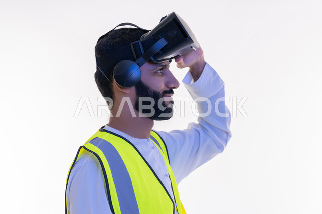 نمو وتطور المجال الهندسي، التفاعل مع الهندسة الافتراضية، بورتريه مقرب من الجانب لمهندس عربي خليجي إماراتي يرتدي الكندورة والسترة الخاصة بالعمل يضع نظارة الواقع الافتراضي على رأسه، دمج التكنولوجيا بالمجالات الهندسية، رؤية مستقبلية 2030، خلفية بيضاء