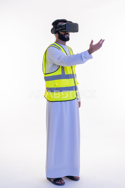دمج التكنولوجيا بالمجالات الهندسية، التفاعل مع الهندسة الافتراضية، بورتريه لمهندس عربي خليجي إماراتي يرتدي الكندورة والسترة الخاصة بالعمل ونظارة الواقع الافتراضي يقوم بحمل عنصر ما، رؤية مستقبلية 2030، نمو وتطور المجال الهندسي، الجسم بالطول الكامل، خلفية بيضاء