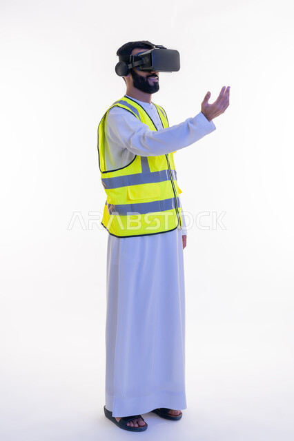رؤية مستقبلية 2030، نمو وتطور المجال الهندسي، التفاعل مع الهندسة الافتراضية، بورتريه لمهندس عربي خليجي إماراتي يرتدي الكندورة والسترة الخاصة بالعمل ونظارة الواقع الافتراضي يقوم بحمل عنصر ما، دمج التكنولوجيا بالمجالات الهندسية، الجسم بالطول الكامل، خلفية بيضاء