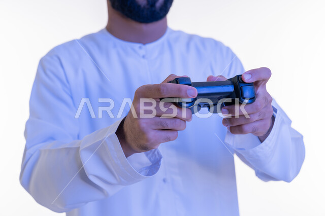 قضاء أوقات الفراغ بأنشطة ممتعة، استخدام الأجهزة التكنولوجية والتقنيات الحديثة، بورتريه مقرب لرجل عربي خليجي اماراتي يرتدي الكندورة  الإماراتية يمسك بيديه عصا التحكم، اللعب بألعاب الفيديو الترفيهية, خلفية بيضاء