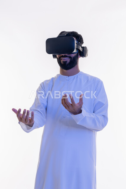 الاندماج والتفاعل ومحاكاة العالم الخيالي، بورتريه لشاب عربي إماراتي يرتدي الكندورة ونظارة في آر الافتراضية ثلاثية الأبعاد يحاول الامساك بشيء ما، استخدام حاسة اللمس لملامسة عناصر هولوجرامية بإيماءات النقر, خلفية بيضاء