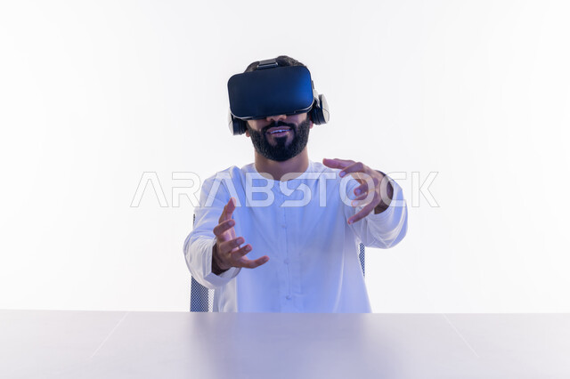 دمج التسلية مع العالم الخيالي عبر التقنيات الحديثة، بورتريه مقرب لرجل عربي خليجي إماراتي يرتدي الكندورة الاماراتية ويضع نظارة ثلاثية الأبعاد، الاستمتاع بمشاهدة أفلام الواقع الافتراضي، استخدام حاسة اللمس لتحريك العناصر، تعابير السعادة والسرور ، خلفية بيضاء
