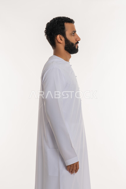 Caring about appearance, the concept of elegance, masculinity and strength, a side portrait of an Arab Gulf Emirati man wearing the Emirati kandura looking at something, standing straight and steady and looking to the right with gestures of self-confidence, expressions of seriousness and firmness, white background