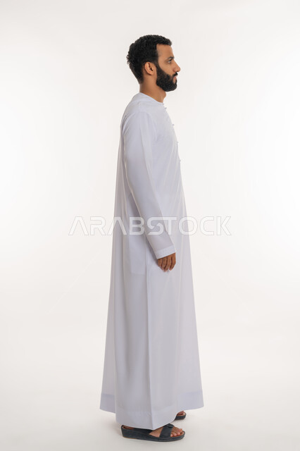تعابير الجدية والحزم، الاهتمام بالمظهر الخارجي، مفهوم الأناقة والرجولة والقوة, بورتريه من الجانب لرجل عربي خليجي إماراتي يرتدي الكندورة الاماراتية تنظر الى شيء ما, الوقوف باستقامة وثبات والنظر الى اليمين بايماءات الثقة بالنفس, الطول الكامل للجسم, خلفية بيضاء
