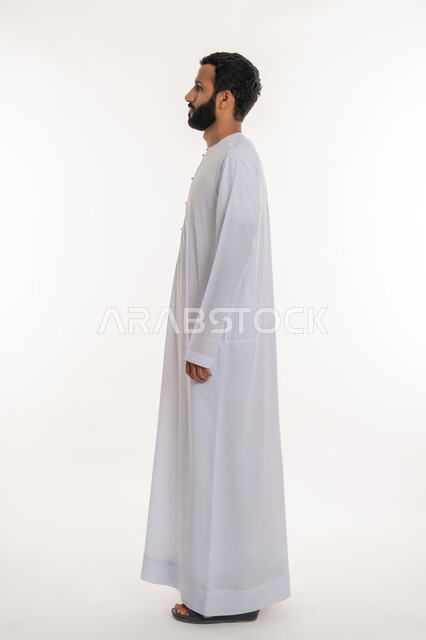 الوقوف باستقامة وثبات والنظر الى اليمين بايماءات الثقة بالنفس, تعابير الجدية والحزم، الاهتمام بالمظهر الخارجي، مفهوم الأناقة والرجولة والقوة, بورتريه من الجانب لرجل عربي خليجي إماراتي يرتدي الكندورة الاماراتية ينظر الى شيء ما, الطول الكامل للجسم، خلفية بيضاء