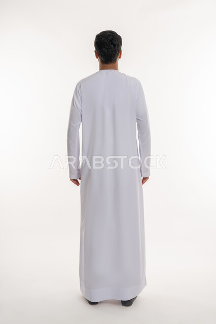 مفهوم الرجولة والقوة، الأناقة والاهتمام بالمظهر الخارجي، بورتريه من الخلف لرجل عربي خليجي إماراتي يرتدي الكندورة الاماراتية ينظر إلى شي ما، الوقوف باستقامة وثبات، الاعتراض عن موضوع محدد، الطول الكامل للجسم، خلفية بيضاء