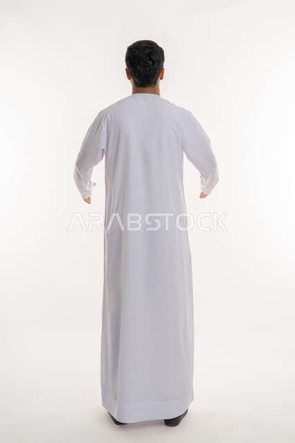 الاعتراض عن موضوع محدد، مفهوم الرجولة والقوة، الأناقة والاهتمام بالمظهر الخارجي، بورتريه من الخلف لرجل عربي خليجي إماراتي يرتدي الكندورة الاماراتية ينظر إلى شي ما، الوقوف باستقامة وثبات، الطول الكامل للجسم، خلفية بيضاء