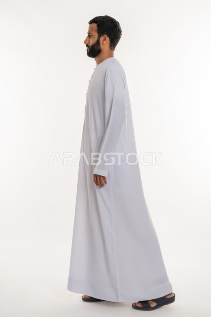 ايماءات المشي و الذهاب إلى مكان معين، بورتريه من الجانب لرجل عربي خليجي إماراتي يرتدي الكندورة ينظر إلى شيء ما، التقدم إلى الأمام بخطوات ثابتة، تعابير الجدية والحزم، الاهتمام بالمظهر الخارجي، مفهوم الأناقة والرجولة والقوة, الطول الكامل للجسم، خلفية بيضاء