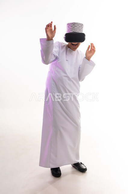 التطور التقني والتكنولوجي, النظر الى الافلام الواقعيه ومحاكاة العالم الخيالي ، المتعة و التسلية بالمشاهدة عبر نظارة الواقع الافتراضي،  بورتريه لولد عربي خليجي عماني يرتدي الدشداشه والكمه ينظر من خلال نظارات ثلاثية الأبعاد (الفي ار)، الجسم بالطول الكامل، خلفيه بيضاء