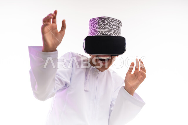 Fun and entertainment by watching through virtual reality glasses, technical and technological development, watching real movies and simulating the imaginary world, portrait of an Arab Gulf Omani boy wearing a dishdasha and a cloak looking through 3D glasses (VR), white background