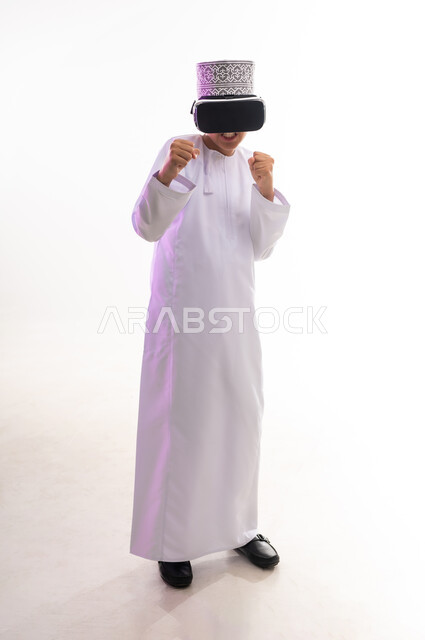المتعة و التسلية بالمشاهدة عبر نظارة الواقع الافتراضي، التطور التقني والتكنولوجي, بورتريه لولد عربي خليجي عماني يرتدي الدشداشه والكمه ينظر من خلال نظارات ثلاثية الأبعاد (الفي ار), محاكاة العالم الخيالي والنظر الى الافلام الواقعيه، الجسم بالطول الكامل، خلفيه بيضاء