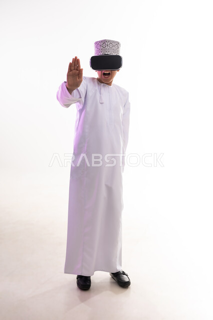 طلب التوقف وعدم الاقتراب, مفهوم الرفض والامتناع, المشاهدة عبر نظارة الواقع الافتراضي، بورتريه لولد عربي خليجي عماني يرتدي الدشداشه والكمه ينظر من خلال نظارات ثلاثية الأبعاد (الفي ار) يرفع كفه للاعلى بإيماءات النهي عن فعل امر ما,  الجسم بالطول الكامل، خلفيه بيضاء