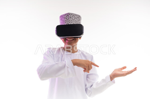 النظر الى الافلام الواقعيه والتفاعل والاندماج ومحاكاة العالم الخيالي ، استخدام التقنيات والأجهزة المتطورة، بورتريه لولد عربي خليجي عماني يرتدي الدشداشه والكمه ينظر من خلال نظارات ثلاثية الأبعاد (الفي ار) يشير باصبع السبابة الى مكان ما,  خلفيه بيضاء