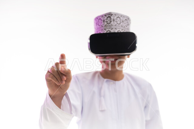 الاندماج ومحاكاة العالم الخيالي والنظر الى الافلام الواقعيه، استخدام التقنيات والأجهزة المتطورة، بورتريه لولد عربي خليجي عماني يرتدي الدشداشه والكمه ينظر من خلال نظارات ثلاثية الأبعاد (الفي ار) يشير باصبع السبابة الى مكان ما,  خلفيه بيضاء