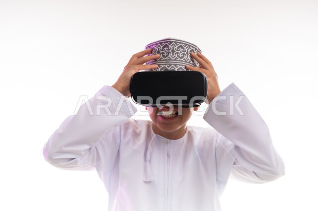 الاندماج ومحاكاة العالم الخيالي، المتعة و التسلية بالمشاهدة عبر نظارة الواقع الافتراضي، التطور التقني والتكنولوجي, بورتريه لولد عربي خليجي عماني يرتدي الدشداشه والكمه ينظر من خلال نظارات ثلاثية الأبعاد (الفي ار),  خلفيه بيضاء