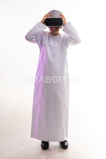 المتعة والتسلية بالمشاهدة عبر نظارة الواقع الافتراضي، التطور التقني والتكنولوجي,  بورتريه لولد عربي خليجي عماني يرتدي الدشداشه والكمه ينظر من خلال نظارات ثلاثية الأبعاد (الفي ار), الاندماج ومحاكاة العالم الخيالي والنظر الى الافلام الواقعيه، الجسم بالطول الكامل، خلفيه بيضاء