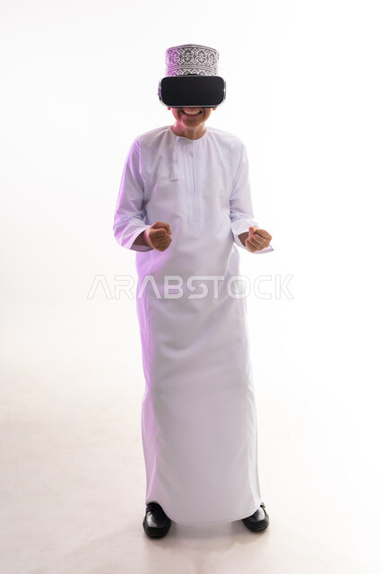 Technical and technological development, fun and entertainment by watching through virtual reality glasses, portrait of an Arab Gulf Omani boy wearing a dishdasha and a kimono looking through 3D glasses (VR), merging and simulating the imaginary world and watching real movies, full-length body, white background