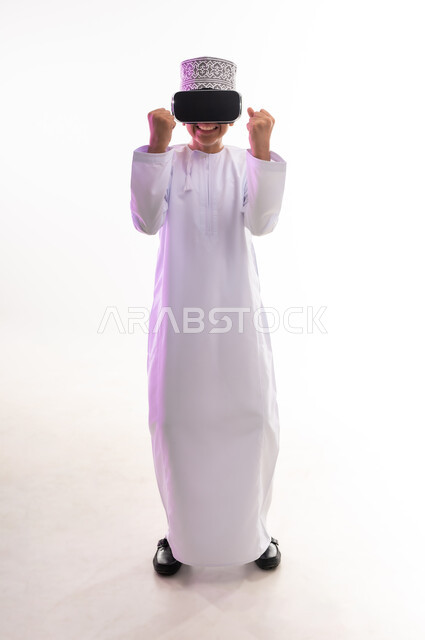 Fun and entertainment by watching through virtual reality glasses, technical and technological development, portrait of an Arab Gulf Omani boy wearing a dishdasha and a kimono looking through 3D glasses (VR), simulating the imaginary world and watching real movies, full-length body, white background