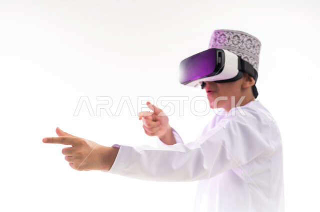 رفع اليد بإيماءات الاندماج ومحاكاة العالم الخيالي، المتعة و التسلية بالمشاهدة عبر نظارة الواقع الافتراضي، التطور التقني والتكنولوجي, بورتريه لولد عربي خليجي عماني يرتدي الدشداشه والكمه ينظر من خلال نظارات ثلاثية الأبعاد (الفي ار),  خلفيه بيضاء