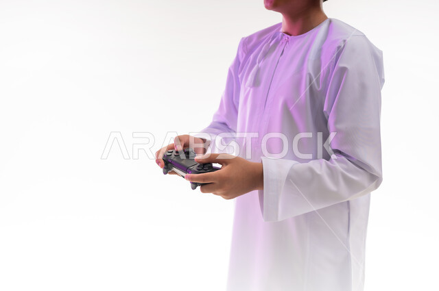 قضاء أوقات ممتعة في ألعاب الفيديو الترفيهيه، بورتريه لولد عربي خليجي عماني يرتدي الدشداشة والكمة يحمل بيده عصا التحكم، إيماءات الاستمتاع والاندماج، استخدام الأجهزة التكنولوجية والتقنيات الحديثة، خلفية بيضاء