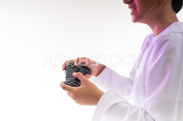 قضاء أوقات ممتعة في ألعاب الفيديو الترفيهيه، بورتريه لولد عربي خليجي عماني يرتدي الدشداشة والكمة يحمل بيده عصا التحكم، إيماءات الاستمتاع والاندماج، استخدام الأجهزة التكنولوجية والتقنيات الحديثة، خلفية بيضاء