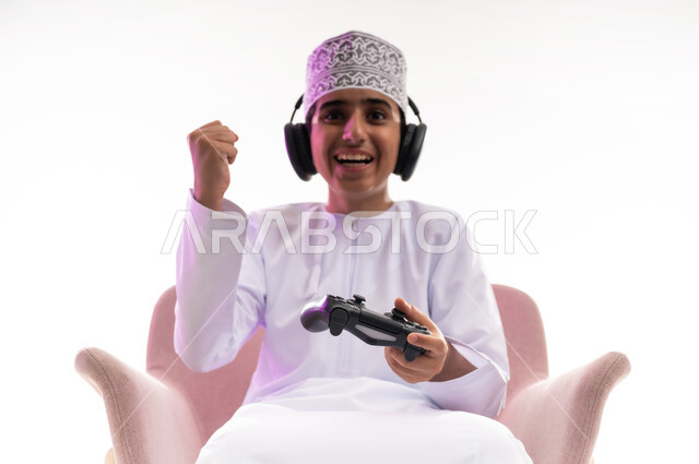 Artistic singing talents, interaction with musical tunes, the concept of listening and enjoying, listening to songs using headphones, spending fun times playing video games, a portrait of an Arab Gulf Omani boy wearing a dishdasha and a turban, wearing headphones and holding a joystick in his hand, white background