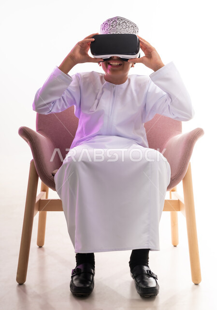 تعابير الاندماج والتركيز، محاكاة العالم الخيالي والنظر الى الافلام الواقعيه، التطور التقني والتكنولوجي، بورتريه لولد عربي خليجي عماني يرتدي الدشداشه والكمه ينظر من خلال نظارات ثلاثية الأبعاد (الفي ار),  الجسم بالطول الكامل، خلفيه بيضاء