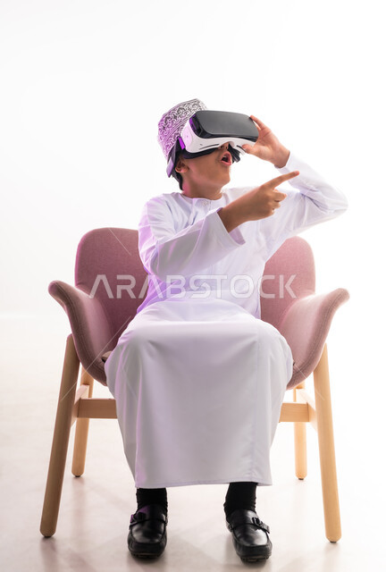 Fun and entertainment by watching through virtual reality glasses, merging and simulating the imaginary world, portrait of an Arab Gulf Omani boy wearing a dishdasha and a kimono, looking through 3D glasses (VR), pointing with his index finger to a place, full-length body, white background
