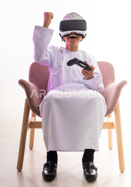 قضاء أوقات ممتعة في ألعاب الفيديو الترفيهيه، الاندماج ومحاكاة العالم الخيالي، استخدام الأجهزة التكنولوجية والتقنيات الحديثة، بورتريه لولد عربي خليجي عماني يرتدي الدشداشه والكمه ينظر من خلال نظارات ثلاثية الأبعاد (الفي ار) يمسك بيده عصا التحكم,  خلفيه بيضاء