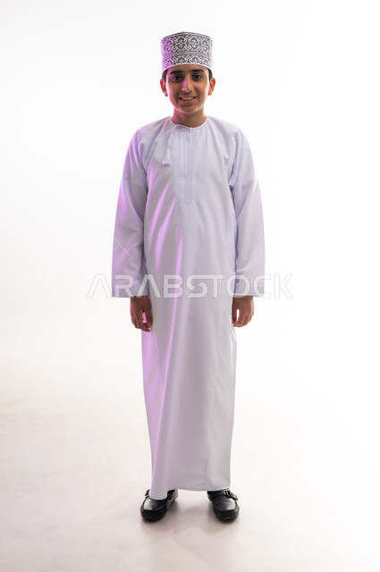 الرجولة والثقة بالنفس،  التقاط الصور الشخصية للوثائق الرسمية،  الاهتمام بالأناقة والمظهر الخارجي، بورتريه لولد عربي خليجي عماني مبتسم يرتدي الدشداشة و الكمه ينظر الى الكاميرا بإيماءات السرور والسعادة، الجسم بالطول الكامل، خلفية بيضاء