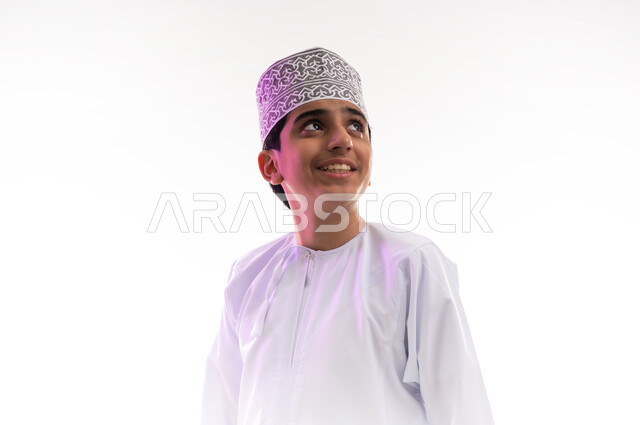 التقاط الصور الشخصية للوثائق الرسمية، مفهوم الرجولة والثقة بالنفس، الاهتمام بالأناقة والمظهر الخارجي، بورتريه مقرب لولد عربي خليجي عماني مبتسم يرتدي الدشداشة و الكمه ينظر الى شيء ما بإيماءات السرور والسعادة، خلفية بيضاء
