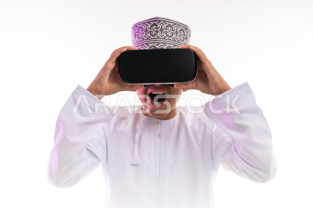 الاندماج ومحاكاة العالم الخيالي والنظر الى الافلام الواقعيه، المتعة و التسلية بالمشاهدة عبر نظارة الواقع الافتراضي، التطور التقني والتكنولوجي,  بورتريه لولد عربي خليجي عماني يرتدي الدشداشه والكمه ينظر من خلال نظارات ثلاثية الأبعاد (الفي ار),   خلفيه بيضاء