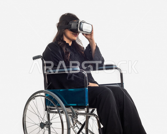 بورتريه لمرأة عربية خليجية سعودية، ، تنظر من خلال نظارات الواقع الإفتراضي (VR Box) ، مقعدة على كرسي متحرك ، الاعاقة الحركية ، خلفية بيضاء ، مفهوم ذوي الإحتياجات الخاصة ، ذوي الهمم ، التكنلوجيا المتطورة ، التسليه والترفيه