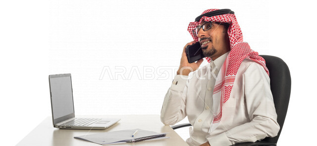 بورتريه لرجل أعمال خليجي سعودي في مقر العمل، إستخدام الحاسوب المحمول لإنجاز المهام، عقد إجتماع عمل عبر الإنترنت، العمل عن بعد، جلسة عمل، مفهوم إدارة الأعمال، إجراء مكالمة هاتفية، متابعة ومناقشة العمل، إستخدام أجهزة تقنية حديثة، التسويق الإلكتروني